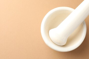 Ceramic mortar and pestle on light brown background, top view. Space for text