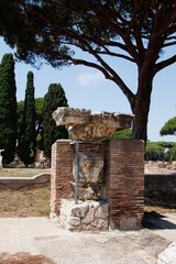 Fototapeta premium OSTIA ANTICA, ITALY, JULY 24, 2022: Ancient Roman ruins with a broken column supported by metal braces, surrounded by brick walls and trees