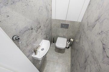 modern, compact bathroom features white fixtures against gray marbled tile walls, with a sleek sink...