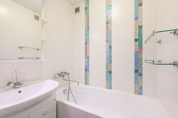 clean bathroom features white tile walls with mosaic strips, a white sink and bathtub. Glass...