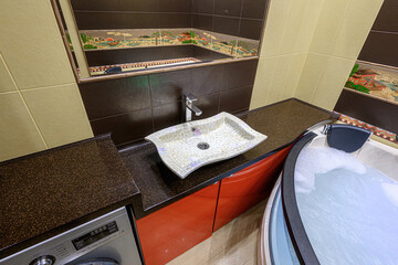 bathroom featuring a unique sink, dark countertops, decorative tilework, and a bubbly bathtub,...