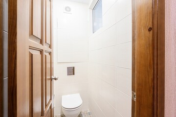 small, bright bathroom with white tiles, a white toilet, and warm-toned wooden doors. Compact and clean