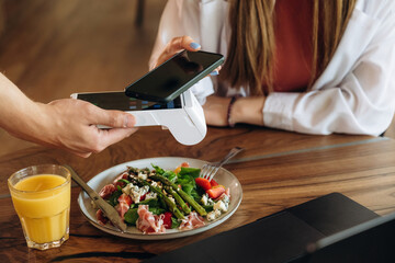 Laptop, salad and orange juice. Woman is paying for meal by wireless payment in the cafe restaurant