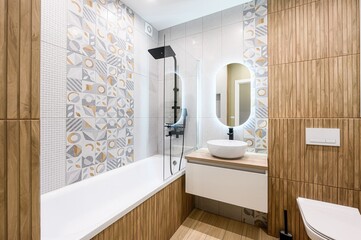 Modern bathroom with geometric tiles, wood panels, and a sleek sink vanity. Features a bathtub with...