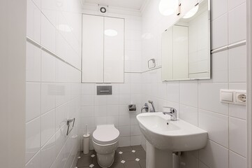 bright bathroom with white square tiles, a toilet, sink, and mirror. The floor is dark gray with white accents. Modern and clean design