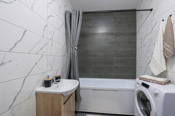 modern bathroom featuring a tub with a gray curtain, a sink with a wooden cabinet, and a washing machine. The walls are tiled in white marble and gray