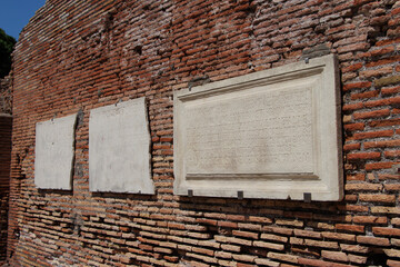 OSTIA ANTICA, ITALY, JULY 24, 2022: Ancient Roman brick wall with three marble plaques inscribed...