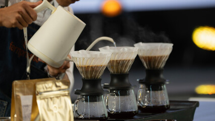 Barista brewing coffee using pour-over method with multiple coffee drippers and steaming coffee.