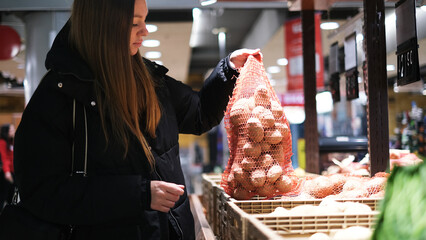 Young woman picking up a bag of potatoes in vegetable section