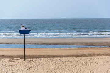 Wooden model of a blue and white boat on pole on a sandy beach, coastal village De Haan, West Flanders, Belgium
