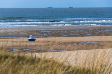 Wooden model of a blue and white boat on pole on a sandy beach, coastal village De Haan, West Flanders, Belgium
