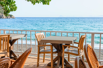 Coastal dining area with wooden chairs overlooking clear blue ocean on a bright sunny day