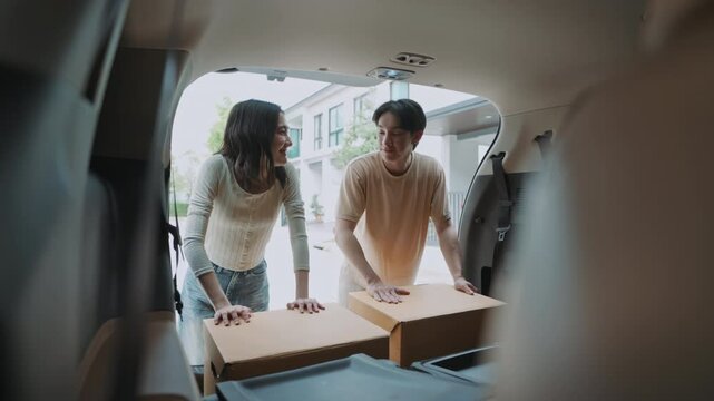 inside car trunk of happy Asian couple loading cardboard boxes. Man and woman smiling, working together on moving day, preparing for relocation to new home. Teamwork and new beginnings.