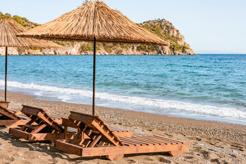 Relaxing beach setup with straw umbrellas and wooden loungers by the calm sea in a picturesque coastal location