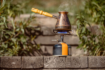 Fragrant coffee steams in copper engraved coffee pot on gas burner with blue flame on wooden bars....