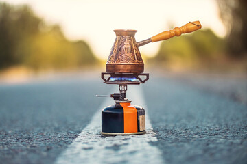 Patterned copper Turkish coffee maker on tourist gas burner with blue flame on highway. Need coffee.