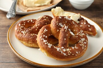 Tasty pretzels with salt and butter on wooden table, closeup