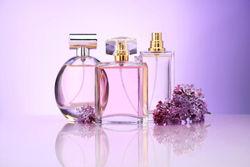 Bottles of perfume and lilac flowers on mirror surface against violet gradient background