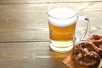 Tasty pretzels and glass mug of beer on wooden table, closeup. Space for text