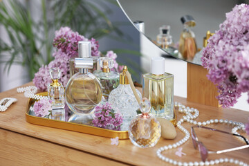 Bottles with perfumes, lilac flowers and accessories on dressing table indoors