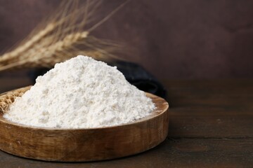 Wheat flour and spikes on wooden table, closeup. Space for text