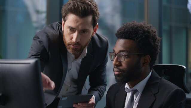 Two multinational businessmen African American Caucasian men diverse males looking pointing at computer monitor pc guys discuss project team working together online business coworkers office employers