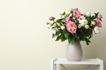 Bouquet of beautiful peony flowers in vase on shelving unit against beige background. Space for text