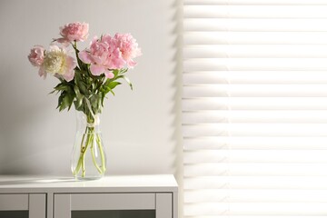 Beautiful peonies in vase on white dresser indoors. Space for text