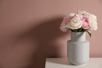 Beautiful peonies in vase on white table near pink wall. Space for text