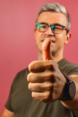 Man giving a thumbs up gesture against a pink background