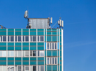 Stacja bazowa telefonii komórkowej na dachu budynku na tle błękitnego nieba.