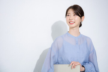 Woman looking up in light blue sheer shirt holding computer with white background Image of recruiter for job change, HR, etc.