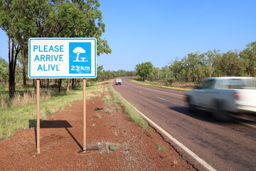 Road sign, please arrive alive. Road safety. Roadside rest area sign, 23km ahead. Fast, speeding car, motion blur. Australia Outback, rural area. Accident, incident, death toll, injuries, statistics