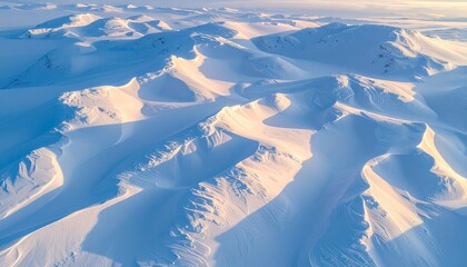Aerial view of snow-covered mountain range in Antarctica illuminated by the soft glow of sunrise, creating a serene and majestic polar landscape.