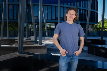 Young man with curly hair standing casually with hands in pockets in modern urban environment. Casual fashion, confident male, contemporary lifestyle concept.