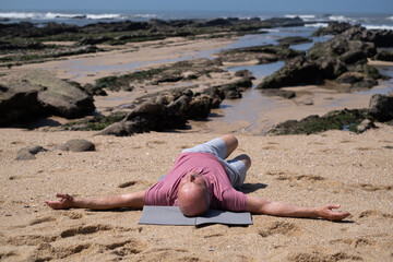 An elderly Spanish man exercising on the beach, stretching his arms.