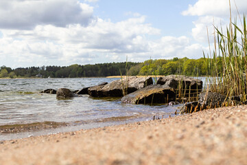 Rocks and coastal reeds meet the gentle waves of the Baltic Sea sandy beach on Vaxholm island, Sweden. A peaceful springtime archipelago view.