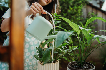 Young woman taking care of plants with water can and mister	

