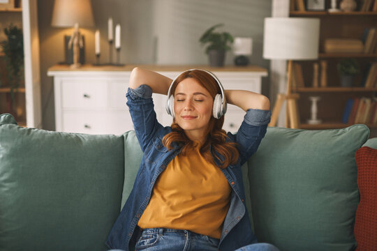 A woman relaxes on a soft couch while wearing headphones, savoring her favorite tunes in a warm and inviting living room filled with natural light.