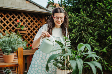 Young woman taking care of plants with water can and mister	
