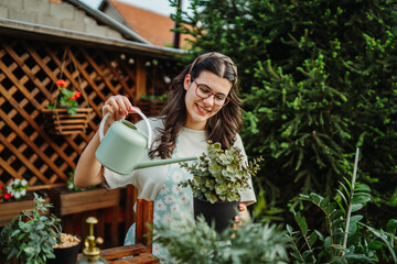Young woman taking care of plants with water can and mister	
