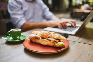 Professionals are engaged in work at a busy cafe, savoring fresh croissants and coffee as they type...