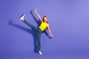 Young woman in vibrant outfit joyfully posing with energetic movement on a purple background...
