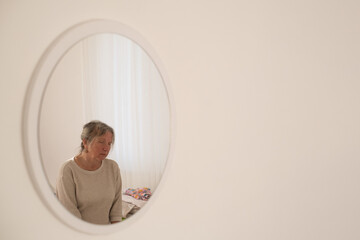 The reflection of a sad elderly woman in the mirror. She is feeling lonely and melancholic.