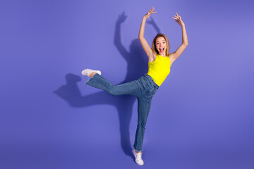 Joyful young woman dancing with enthusiasm in casual attire on a vibrant violet backdrop expressing...