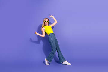 Cheerful young woman in yellow top posing playfully with a vibrant purple backdrop, showcasing a...