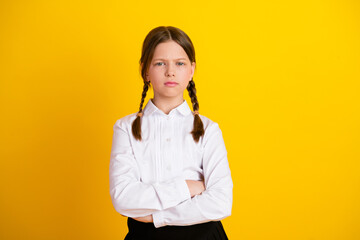 Confident young girl in school uniform standing with crossed arms on a vibrant yellow background