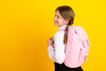 Smiling schoolgirl with pink backpack on yellow background, confidently embracing her school...