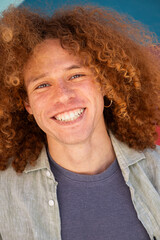 Vertical close-up portrait of smiling young man with curly hair and freckles against colorful wall. Youthful student, personal branding, modern lifestyle and fashion concept.