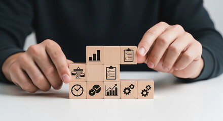 Man's hands arranging wooden blocks with business icons including growth charts, checklist, clock, and gears. Depicts goal setting, planning, time management, and process optimization